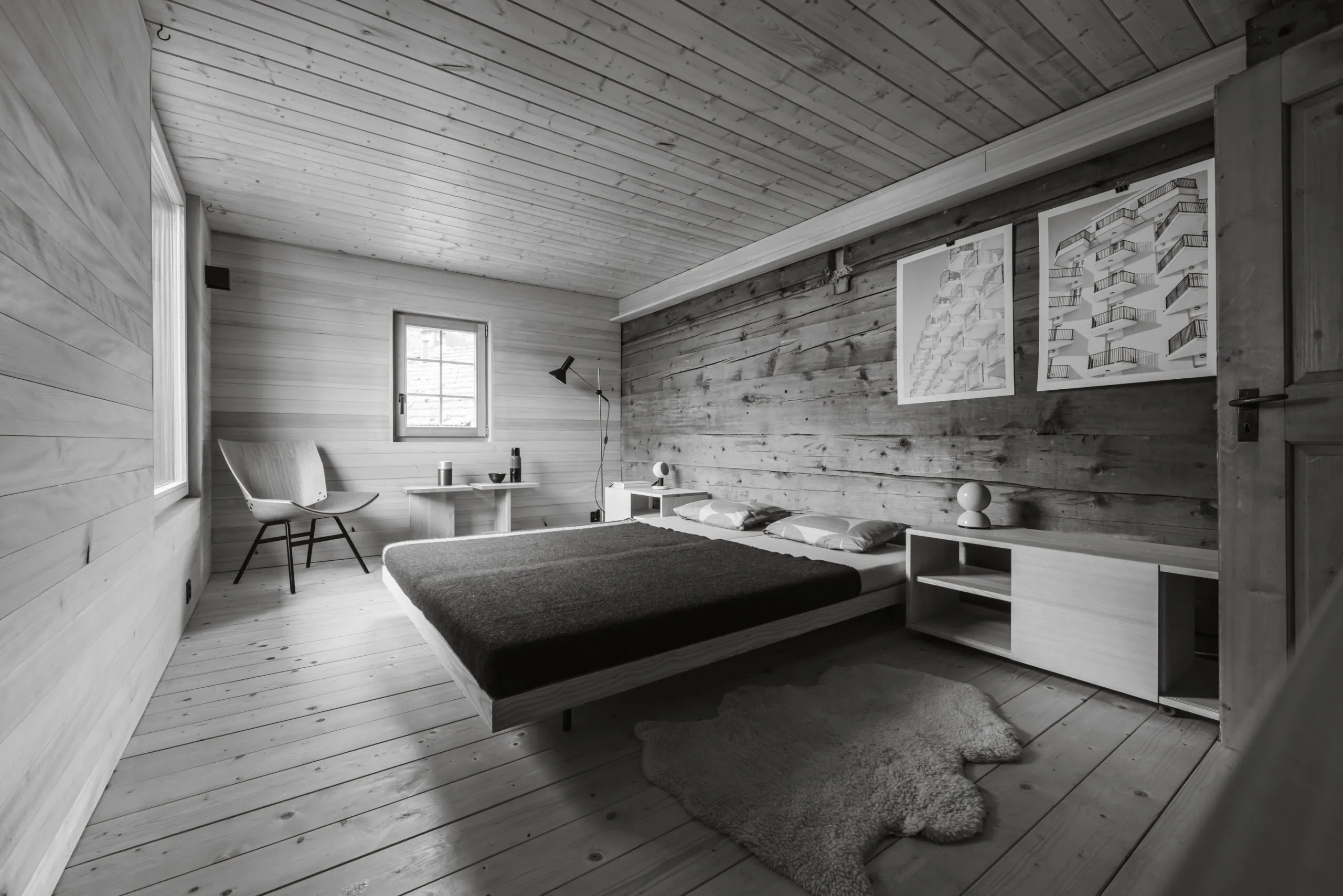 Strickbau: Schlafzimmer mit Bett, Sessel und Bildern an der alten Blockwand