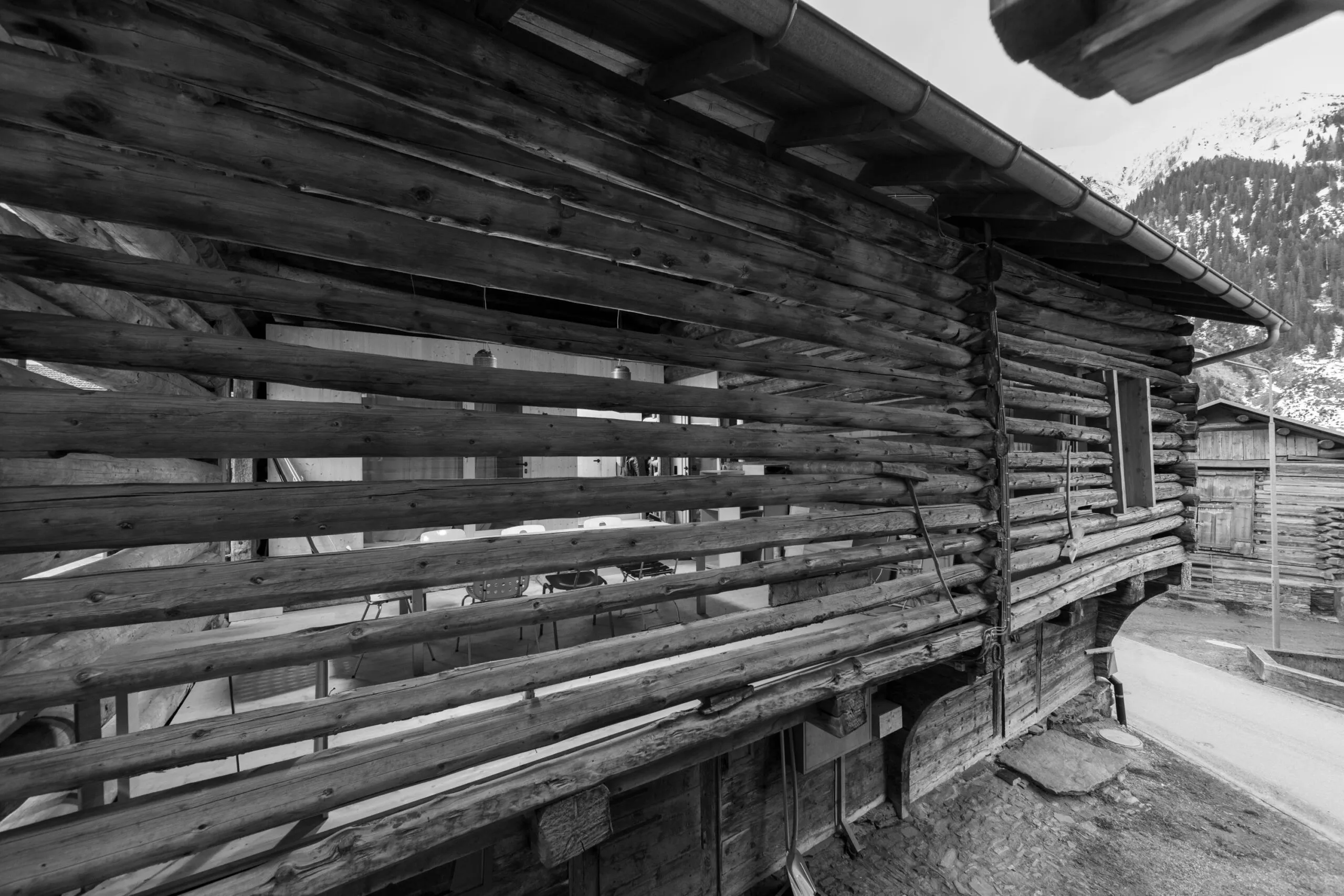 Blick durch die Rundholzwand des Stalls auf Tisch und Stühle dahinter