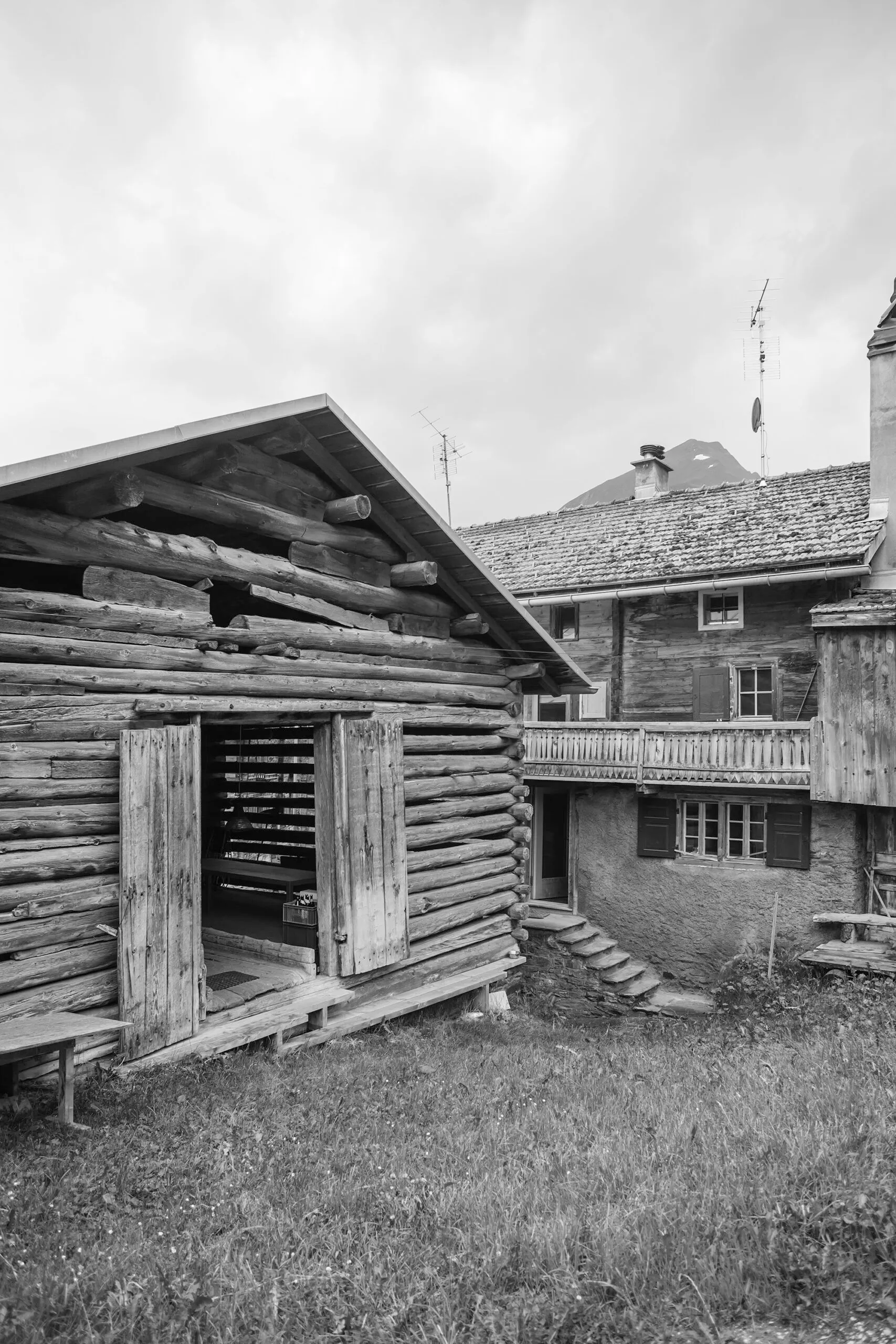 Alter Holzstall mit geöffneter Tür vor einem Wohnhaus in Vrin
